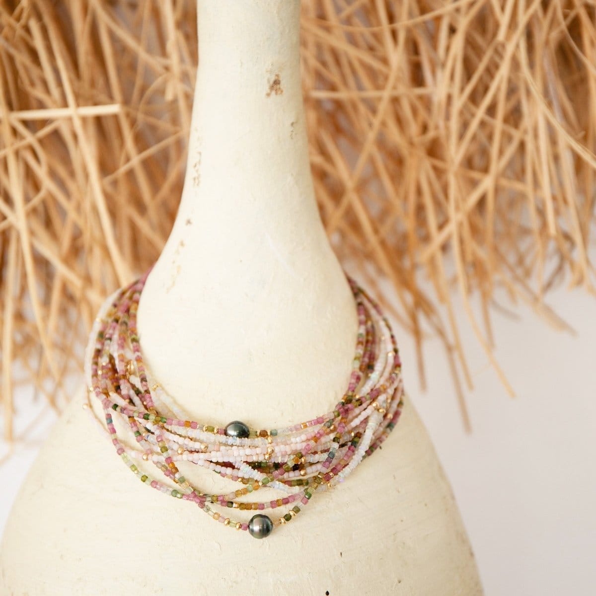 Several Endless Summer Necklaces in Coral Reef, Sweet Escape and Pink Sands around a white ornament with a white and hay grass background.