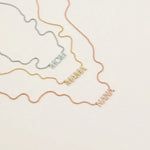 A Pavé MOM Necklace in white gold, a Pavé MAMA Necklace in yellow gold and a Pavé NANA Necklace in rose gold, in a cream background. 