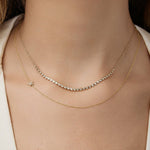 Close-up of a neck wearing The Everyday Diamond Necklace layered with a Custom Gold Necklace - 1 Letter with Pave Star, both in yellow gold, with a white top.