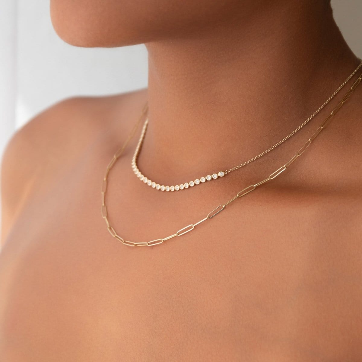 Close-up of a neck wearing The Everyday Diamond Necklace layered with an Element Long Link Chain against a light grey blurred background. 