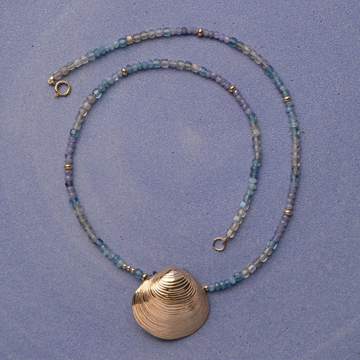 An Endless Summer Necklace - Blue Lagoon and The Golden Venus Shell against a purple background. 