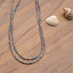 Two Endless Summer Necklaces in Blue Lagoon against a light wooden surface and two shells. 