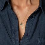 Gold necklace with a blue pendant and diamond 'mommy' pendant worn by a person in a dark shirt.