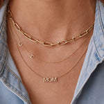 Gold necklaces with 'MOM' pendant and chain necklace on a person wearing a denim shirt.