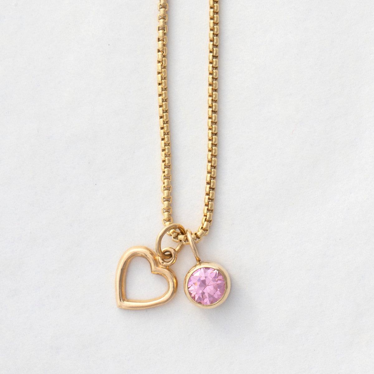A Box Chain with a Cut Out Heart Charm and Color Pop Pendant in Light Pink (Pink Tourmaline) on a light grey background. 
