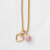 A Box Chain with a Cut Out Heart Charm and Color Pop Pendant in Light Pink (Pink Tourmaline) on a light grey background. 