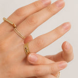 Hand wearing multiple gold rings on a plain background