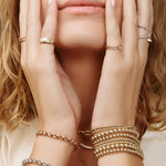 Close-up of hands wearing multiple gold rings and bracelets.