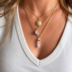 Close-up of a person wearing multiple gold necklaces with various pendants on a white background