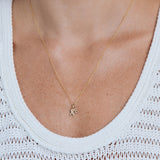Gold necklace with a pendant worn by a person in a white sleeveless top.
