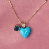 An Etched Turquoise Heart Charm and a Color Pop Pendant in Blue (London Topaz) on a Box Chain against a pink background. 