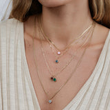 Close-up of a woman wearing an Overboard Layering Chain with a Pink (Pink Tourmaline) Color Pop Pendant, The Slide Chain with a Blue (London Topaz) Color Pop Pendant, an Element Short Link Chain with a Red (Garnet)Color Pop Pendant, Signature Cable Chain with a Green (Lab Grown Emerald) Color Pop Pendant and a Box Chain with a Light Blue (Aquamarine), styled in a cream top. 