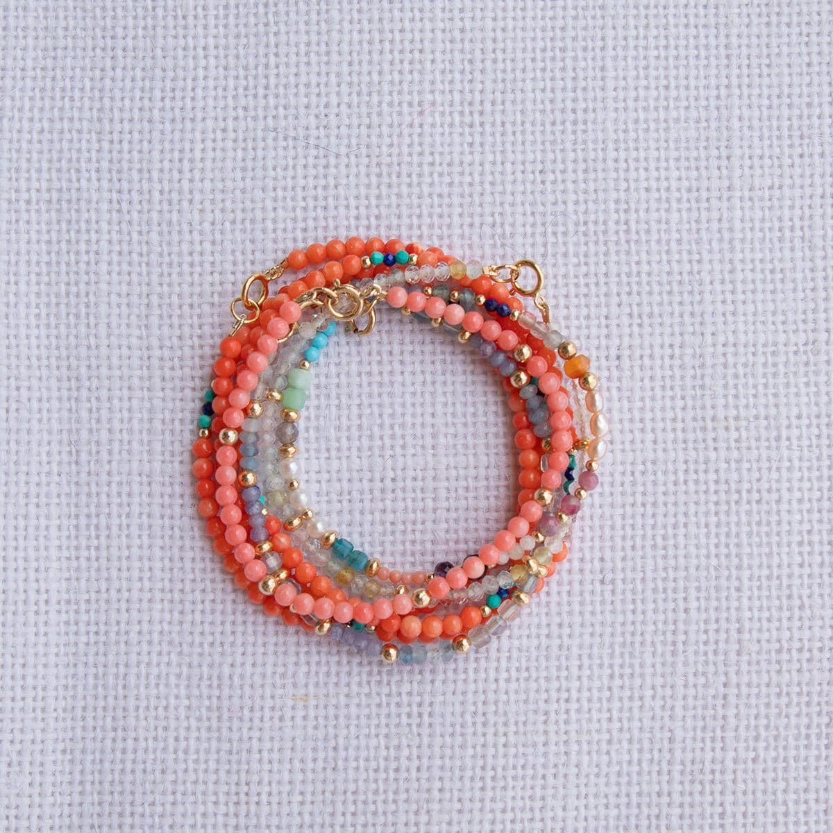 Several Endless Summer Bracelets stacked on a white fabric background. 