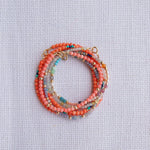 Several Endless Summer Bracelets stacked on a white fabric background. 