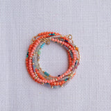 Several Endless Summer Bracelets stacked on a white fabric background. 