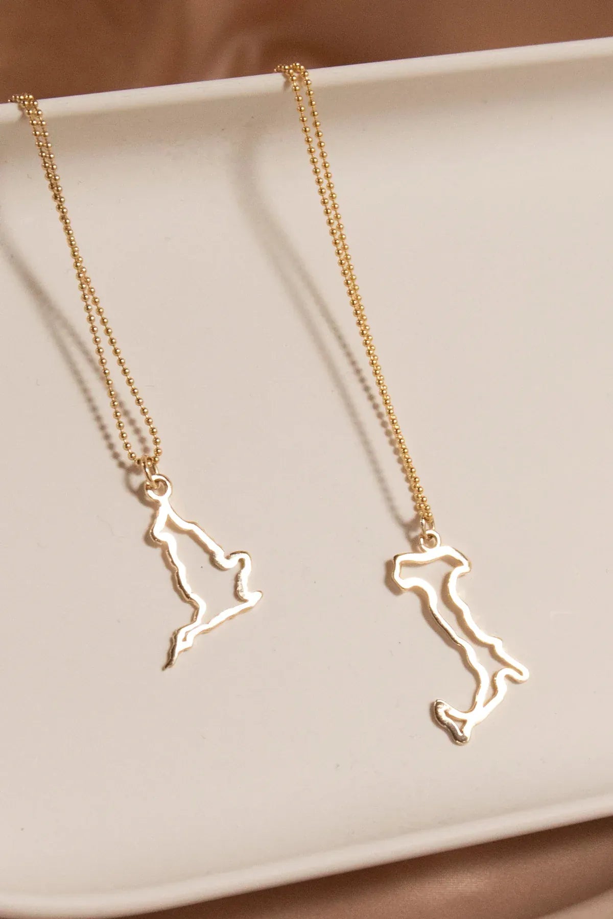 An England Necklace and an Italy Necklace laid on a cream surface against a light brown background.