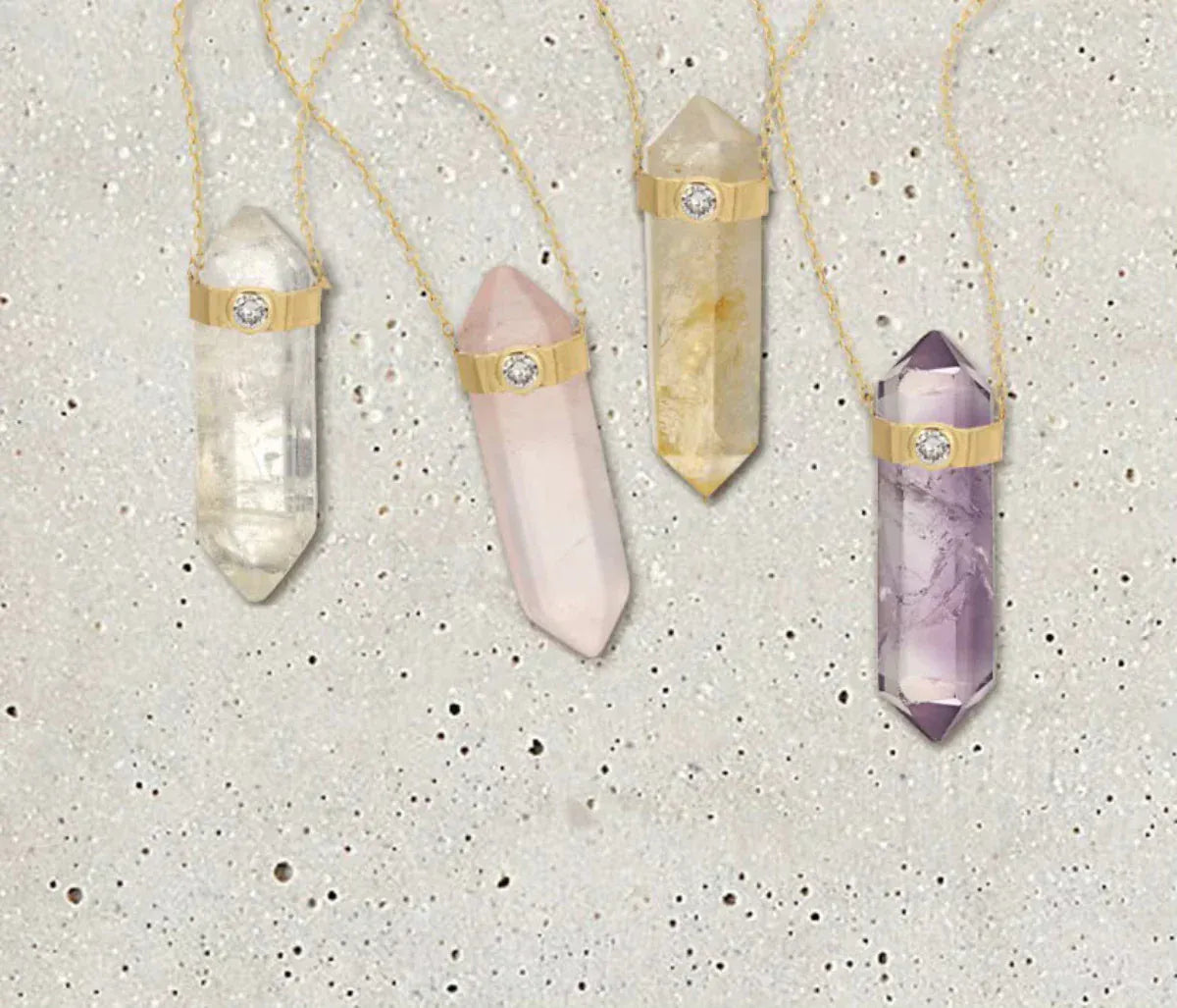 Four The Retreat Necklaces in Clarity, Love, Happiness and Healing on a light grey spotted stone background. 