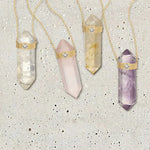 Four The Retreat Necklaces in Clarity, Love, Happiness and Healing on a light grey spotted stone background. 