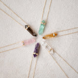 assorted crystal pendants with diamonds on a gold chain on a white fabric background