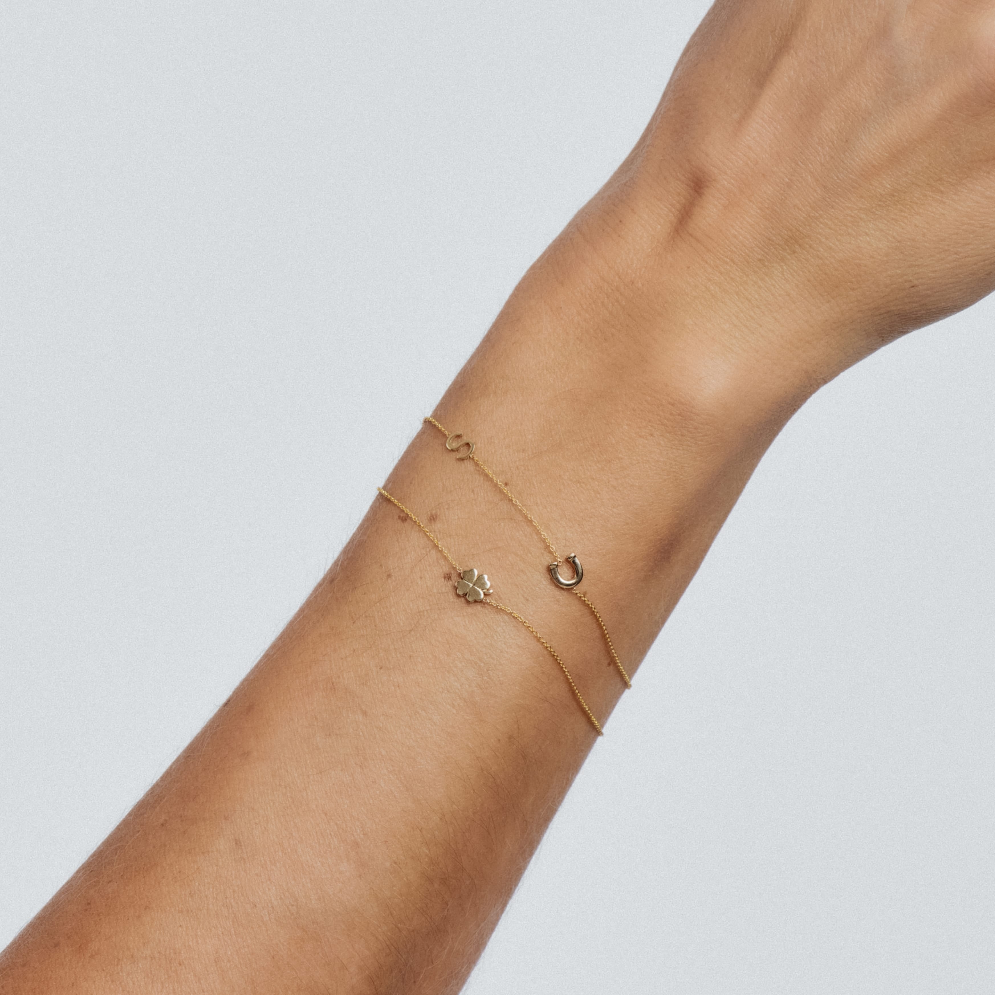 Gold bracelet on a wrist against a light gray background