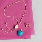 The Slide Heart Bracelet, a Cut Out Heart Charm and an Etched Turquoise Heart Charm on pink tissue paper against a light grey background. 