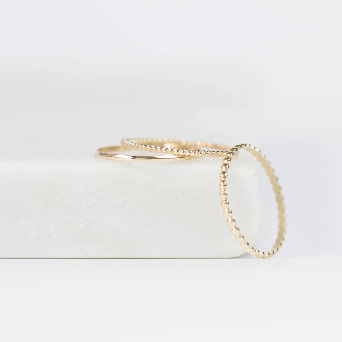 Delicate Trio Stacking Rings in yellow gold on a white surface and background. 