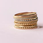 Several Delicate Trio Stacking Rings in yellow gold and white gold on a light pink background. 