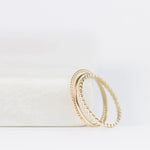Delicate Trio Stacking Rings in yellow gold on a white surface and background. 