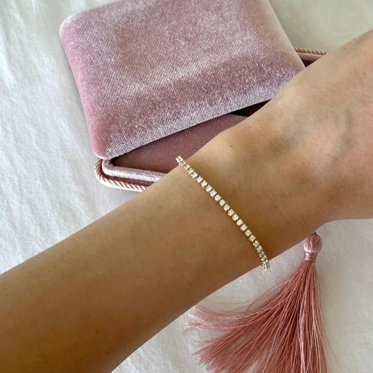 An arm wearing a Tie-Breaker Bracelet with a velvet pink box and tassle in the background. 