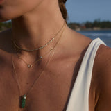Close-up of a person wearing gold necklaces with a green pendant against a blurred natural background