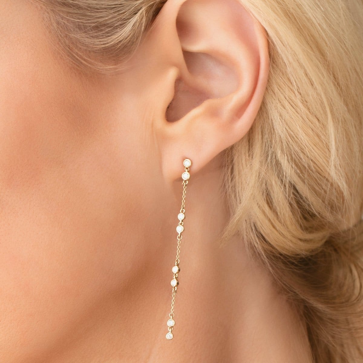Close-up of a Stardust Earring in yellow gold shown on a blonde woman's ear. 