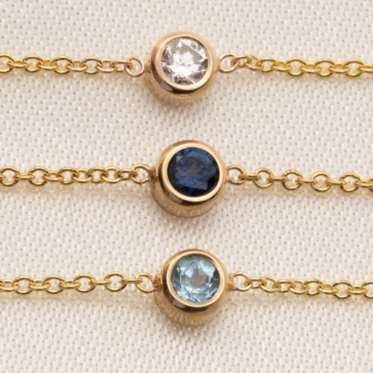 Three gold bracelets with gemstones on a beige fabric background
