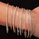 Multiple yellow and white gold  diamond bracelets on a wrist against a black background