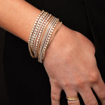 Hand wearing multiple gold diamond tennis bracelets  and gold rings with  on a black background