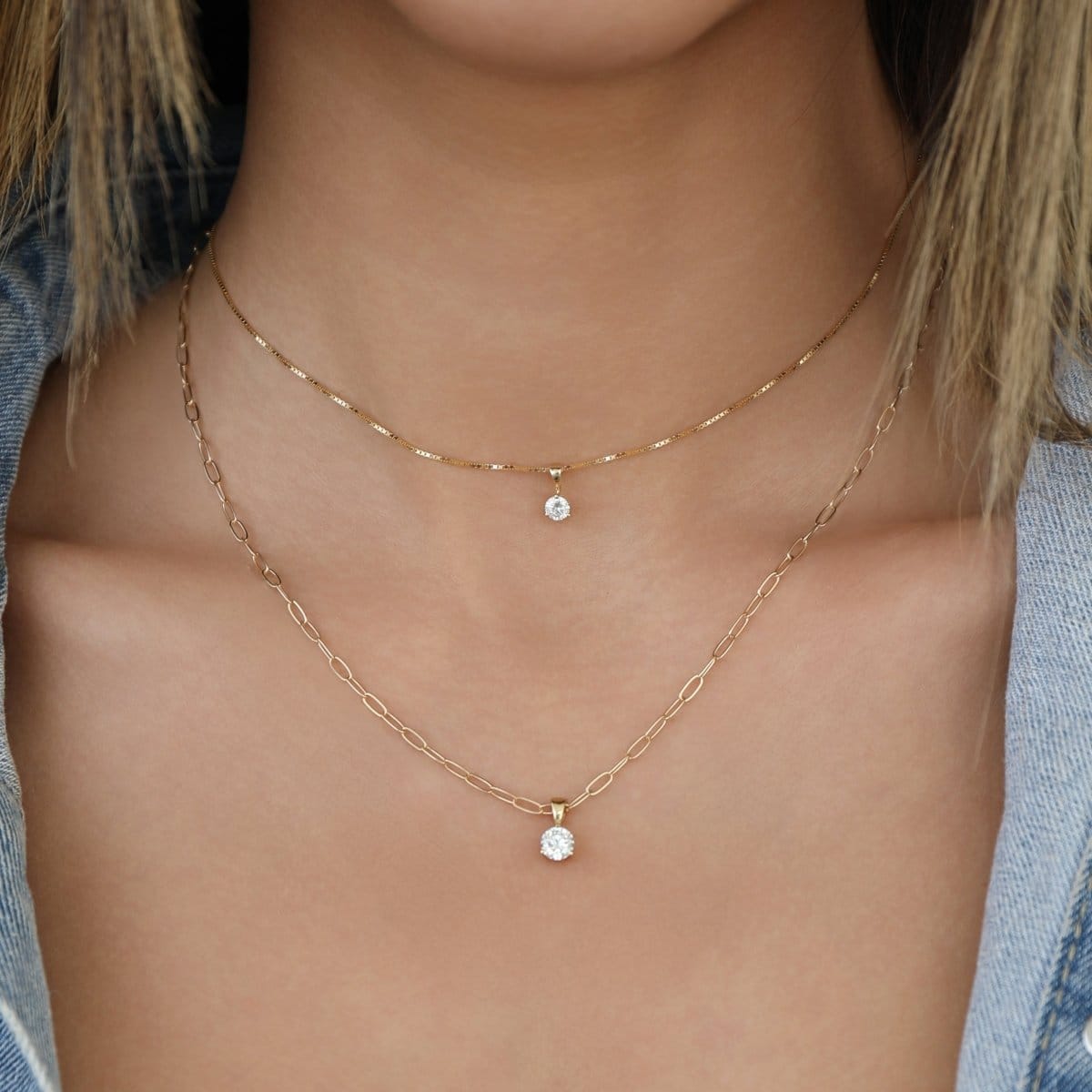 Close-up of a person wearing two gold necklaces with diamond pendants.