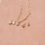 An Element Long Link Chain with Charm Pendants Star, Pave Paw and Pave Heart, and Pave Letter Charms in M and B, against a light pink background. 