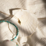 An Endless Summer Necklace - Sea + Sky and Element Short Link Chain with a Golden Spiral Shell on a white shell and white textured fabric. 