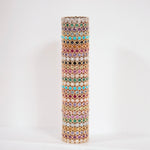 A gold-toned cylindrical colourful eternity rings in pink, green, blue, purple, and white, set against a plain white background.