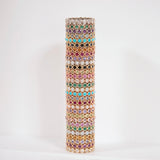 A gold-toned cylindrical colourful eternity rings in pink, green, blue, purple, and white, set against a plain white background.