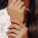 Close-up of a woman's hands wearing several The Evermore Rings, The Magnolia Bouquet Rings, The Lily Bouquet Ring, Open Diamond Ring, 4 Diamond Rings and Pave Diamond Rings, with a white lace top and her brown hair visible. 