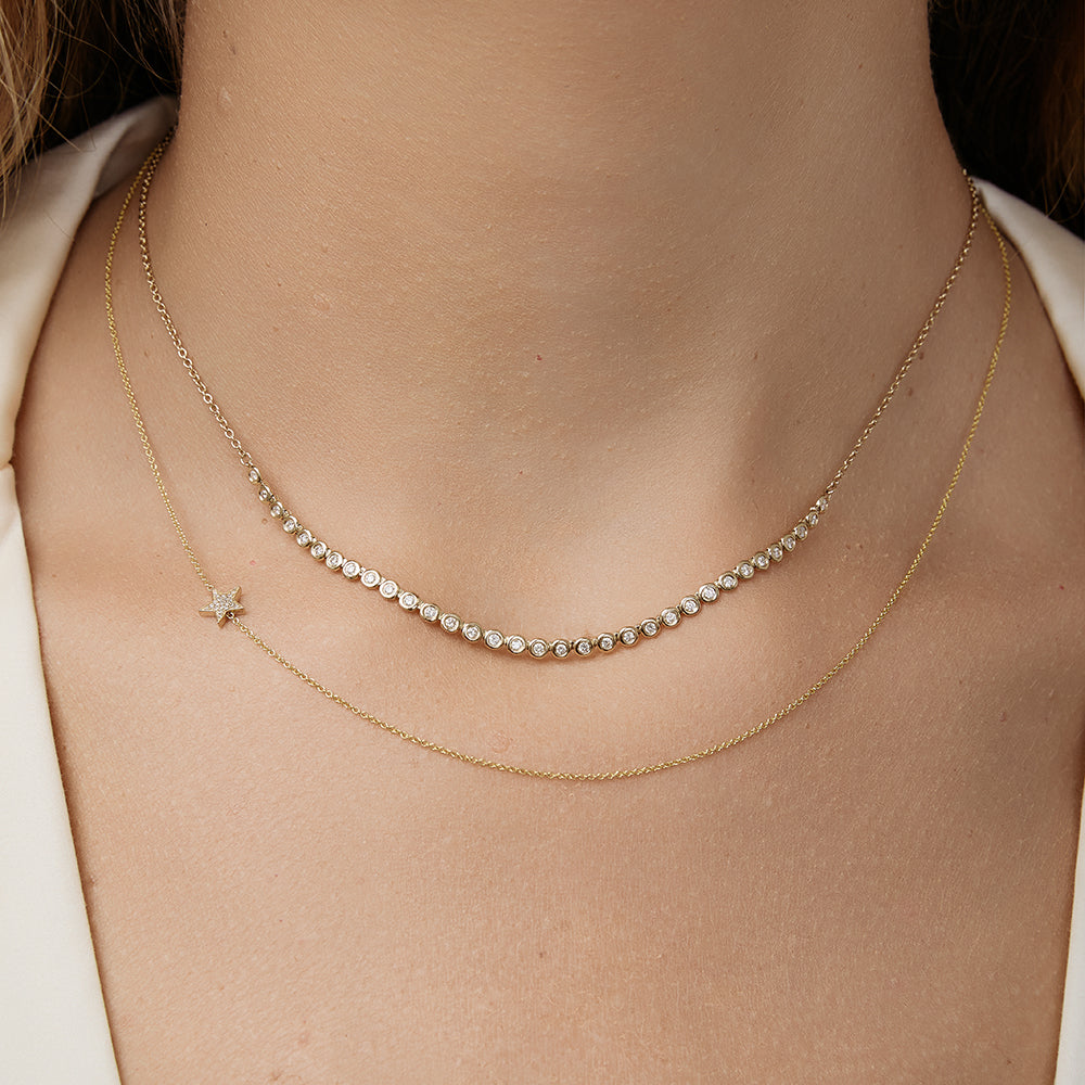 Close-up of a person wearing a diamond necklace layered with a dainty star necklace.