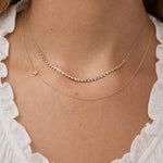 Close-up of a person wearing two gold necklaces with a white lace garment.