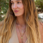 Woman with long blonde hair wearing a Khaki color cord necklace with  a Find Your Way compass pendant outdoors.