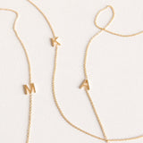 Three gold necklaces with single letter charms, being M, K and A on a plain background. 