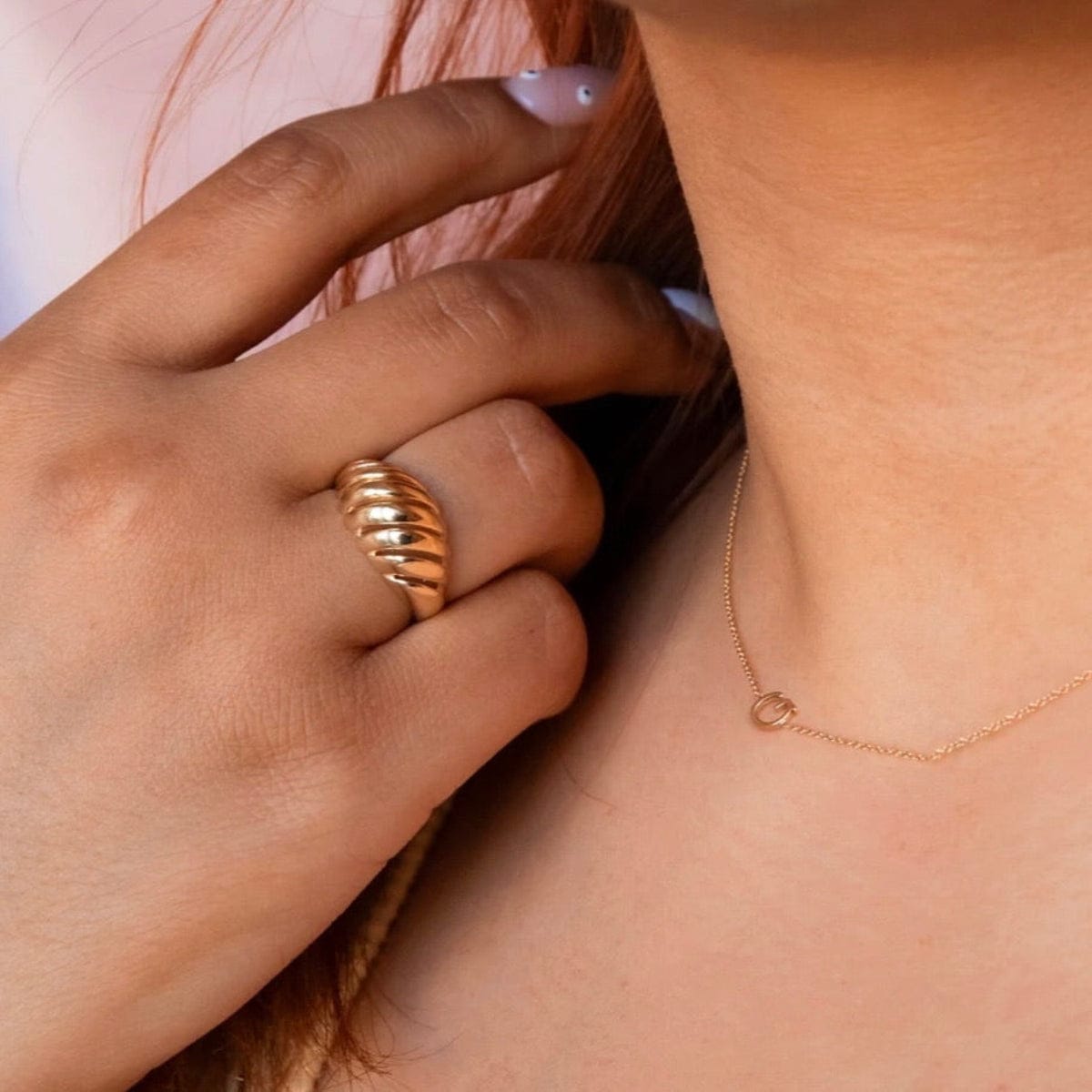 A close-up of a woman's neck and hand wearing a necklace with a letter G charm and a gold statement ring.