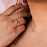 A close-up of a woman's neck and hand wearing a necklace with a letter G charm and a gold statement ring.