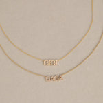 A GIGI Necklace in yellow gold with a cable chain and a Pavé Necklace in yellow gold with a bead chain, against a light beige background. 