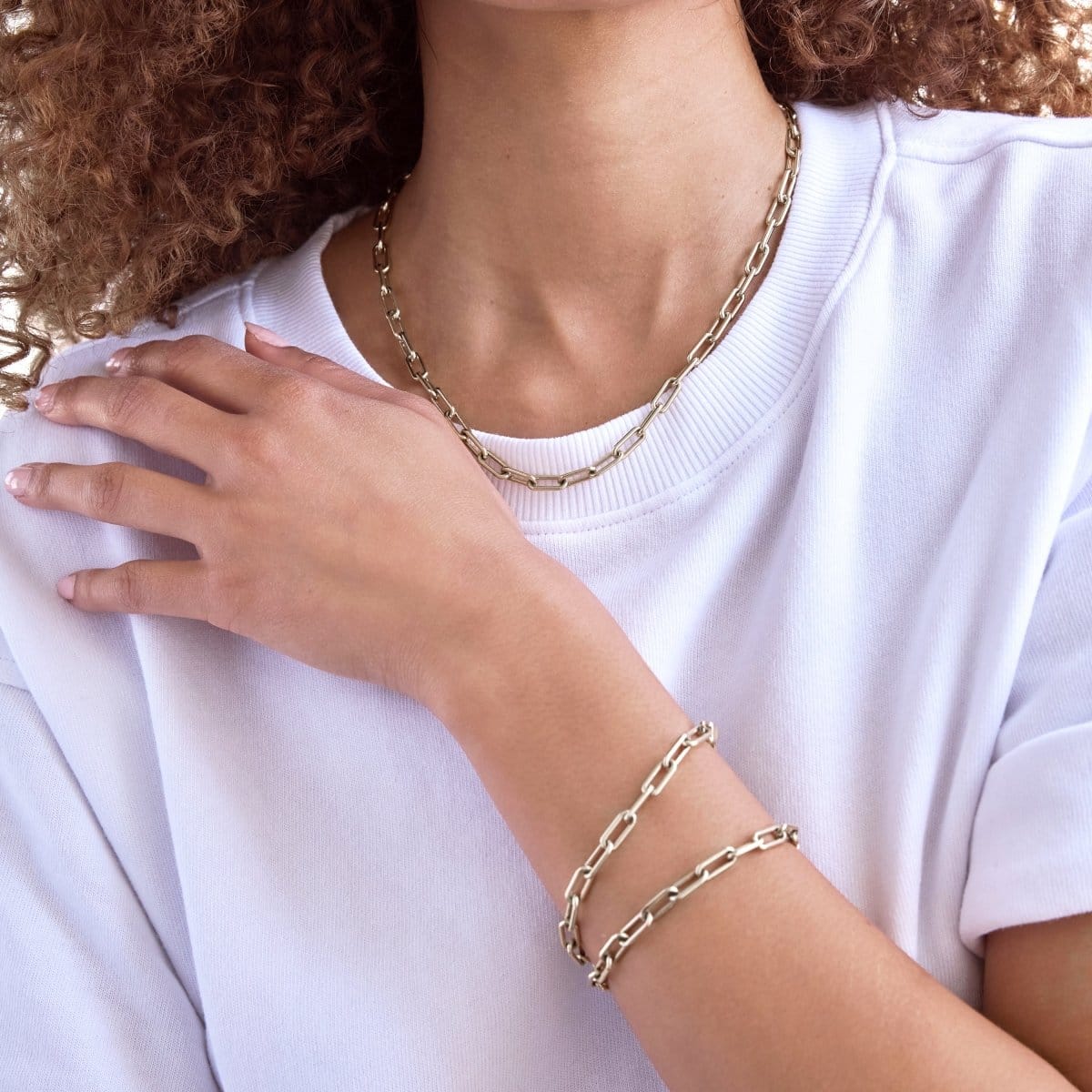 A close-up of a woman wearing a Bold Link Chain and two Bold Link Bracelets, styled with a white t-shirt.