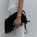 A person wearing an All in Cuff and Plus One Cuff in gold, an Etched Paris Ring in white gold, a C'est Moi Link Ring in rose gold and an Open Diamond Ring in yellow gold, styled in a white top and light grey pants against a textured white background. 