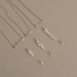Three Petite Name Plate Necklaces with the names Isabella, Louis and Dustin, three Petite Nameplate Pendants in the names Ava, Sophia and Theodore, and three Petite Letter Charms in lowercase a, b and c, all in yellow gold,  against a beige background. 